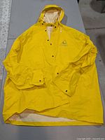Front view of yellow hooded raincoat laid flat showing hood, snaps, logo