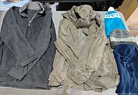 Overview of fleece pullover, hooded jacket, and three headwear items laid on table