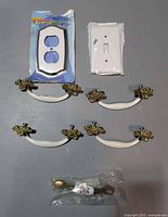Full lot showing four porcelain/brass pulls, packaged outlet cover, loose switch plate, bagged floral pull