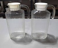 Front view of both ribbed glass pitchers with handles and white flip lids