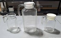 All three ribbed glass pitchers with lids displayed