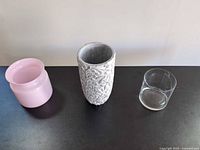 Three of the four containers: pink ceramic vase, white-gray embossed vase, clear glass vase