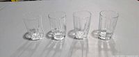 Four clear pressed glass tumblers side by side