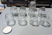 Nine clear glass jars arranged on table, five with metal lids, one extra loose lid