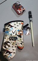 All three items laid out: oven mitt, lightsaber toy, mini tin