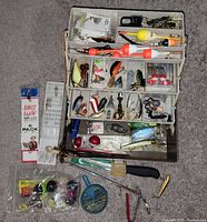 Open tackle box showing lures, bobbers, knives, tools and additional gear placed alongside