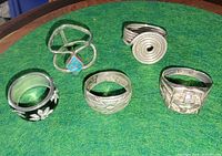 Front angled view of all five sterling silver rings on green surface
