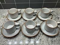 Set of six cups each on a saucer arranged on countertop
