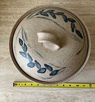 Top view of stoneware casserole with lid showing blue leaf motif and measuring tape for scale