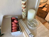 All items grouped on surface: glass place card holders in bowl, wooden napkin rings in box, pillar candle, tapers, match tube