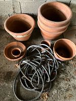 Group shot of all terracotta pots, saucer and coiled hose on floor