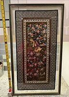 Full view of framed embroidery with tape measure for scale