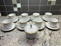 Set of 8 cups, 8 saucers, lidded sugar bowl displayed on countertop