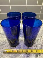 Four cobalt blue glass tumblers standing side by side with tape measure showing height