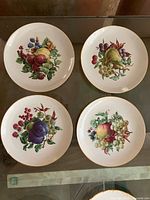 Four ceramic dessert plates, each with different fruit motif and gold rim