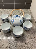 Overhead view of teapot and five cups displaying full set and floral pattern
