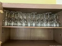 Row of upside-down clear wine glasses in cabinet