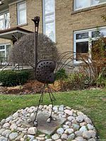 Full view of welded metal bird sculpture on pebble base in garden