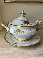 Front view of assembled tureen on underplate showcasing gold floral decoration and shape