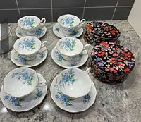 Six teacups and saucers with floral tins on countertop