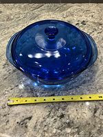 Top view of cobalt blue Pyrex casserole with lid; tape measure shows roughly 10 in. width