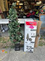 Full view of artificial Nordic fir tree with pinecones in urn next to original box