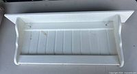 Top view of white wood wall shelf showing beadboard back, curved sides, front rail and hanging hooks