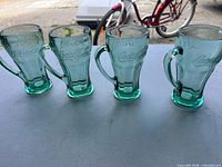 Four green Coca-Cola glass mugs side by side