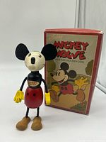 Front view of wooden Mickey Mouse doll standing beside its original box