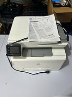 Front angled view of printer with control panel, scanner lid and paperwork visible