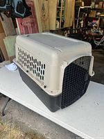Overall view of beige-top black-bottom plastic dog crate with metal front door
