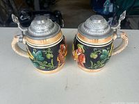 Front view of both steins showing relief tavern and hops scenes