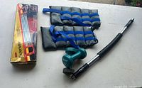 Group shot of all items: chest expander box, ankle weights, dumbbells, power twister bar