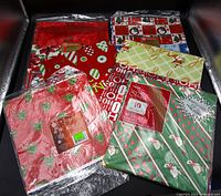 Six gift-wrap packages grouped; holly and Santa stripe packs visible foreground, four additional packs behind