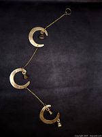 Full view of brass wall hanging showing three crescents linked by chain and bells