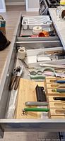 Open drawer showing knife block with knives, mezzaluna, honing steel, cutting board, twine, utensil tray