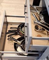 Drawer showing stacked frying pans, saucepan, lids