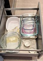 Drawer overview showing nested glass dishes with lids, glass bowls, white oval dish, metal baking sheet and towel