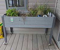 Front view of raised planter showing composite panels, legs, casters, plants and potting mix bag