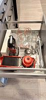 Drawer view showing mandoline, box grater, glass measuring cups, measuring sets, tongs