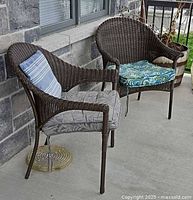 Two wicker patio chairs with cushions and pillow on porch