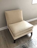 Front three-quarter view of cream armless chair showing overall design and legs