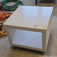 Front view of white square side table showing open compartment and casters