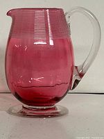 Full view of cranberry glass jug showing body, handle, and foot
