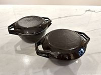 Two chocolate brown enamel Dutch ovens with lids, top view showing textured lids and handles
