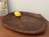 Top view of oval teak carving tray with juice groove and parquet pattern, lemon for scale