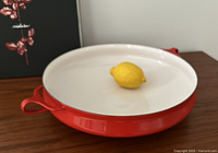 Top view of Dansk red paella pan with white interior and lemon for scale