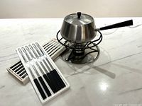 Fondue pot on stand with burner and two trays of fondue forks