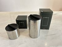 Both stainless canisters with lids and boxes shown