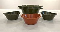Green dutch oven with lid, two green cocottes, one orange cocotte front view